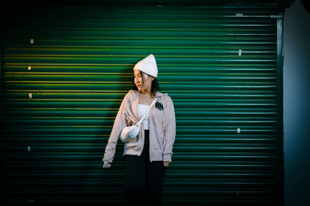 A young woman wearing a white bonnet and hoodie stands against a green roll-up door.