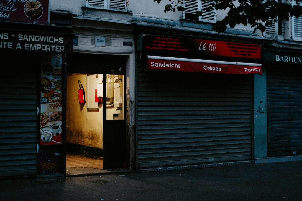 A closed café with a partially open door revealing dim interior lighting, creating a mysterious street scene.