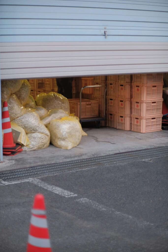 A storage area with packed crates and traffic cones inside a partially opened roll-up door.