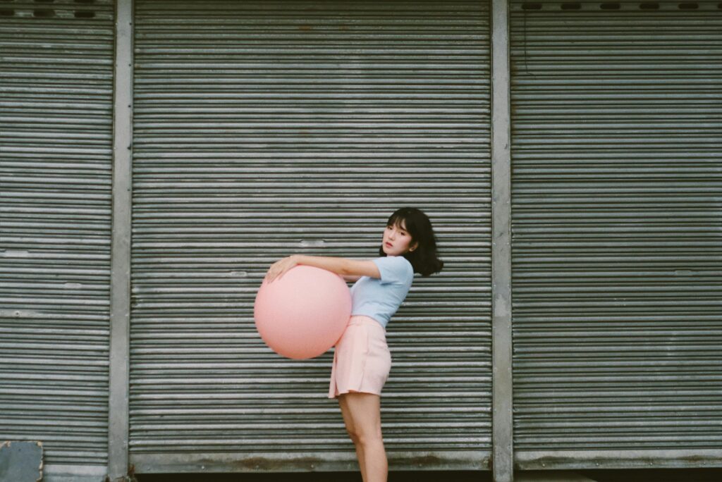 A woman holding a pink balloon in front of a metal roller door, exuding a playful vibe.