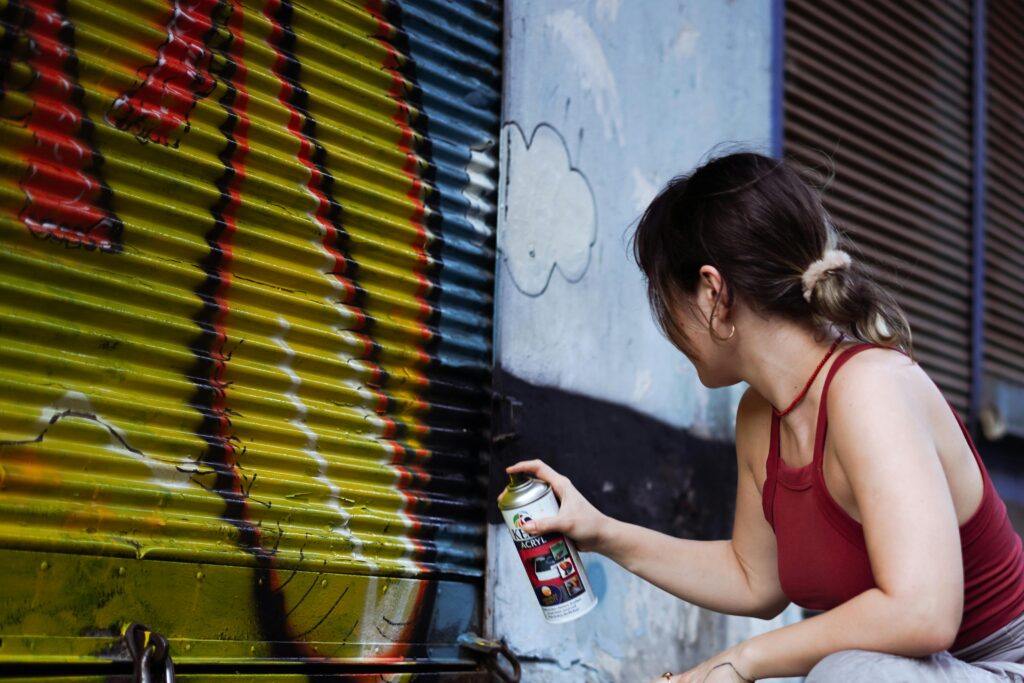 Woman spray painting graffiti on an urban wall, expressing creativity.