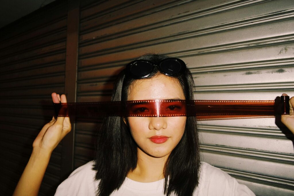 Creative portrait of a woman using a film strip as sunglasses in an urban environment.