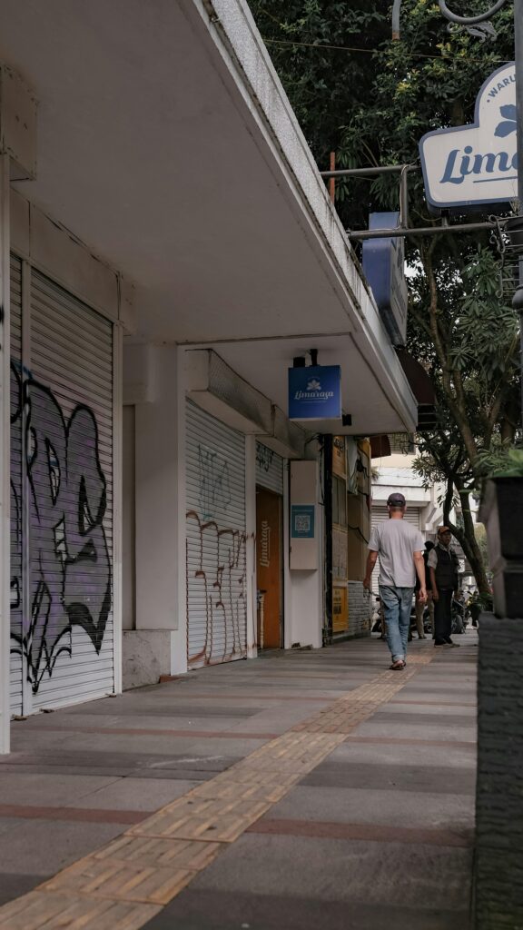 A city sidewalk with graffiti-covered walls, pedestrians, and storefronts captured during the day.