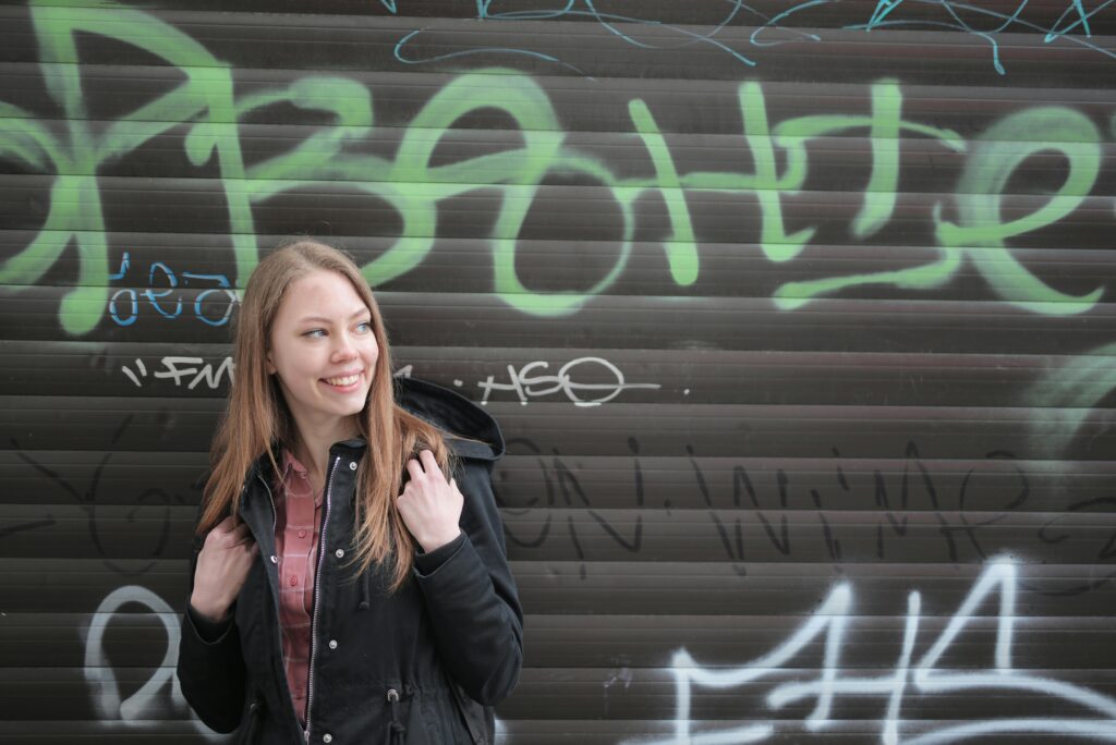 A young woman smiling in front of a graffiti-covered wall. Casual and urban portrait.